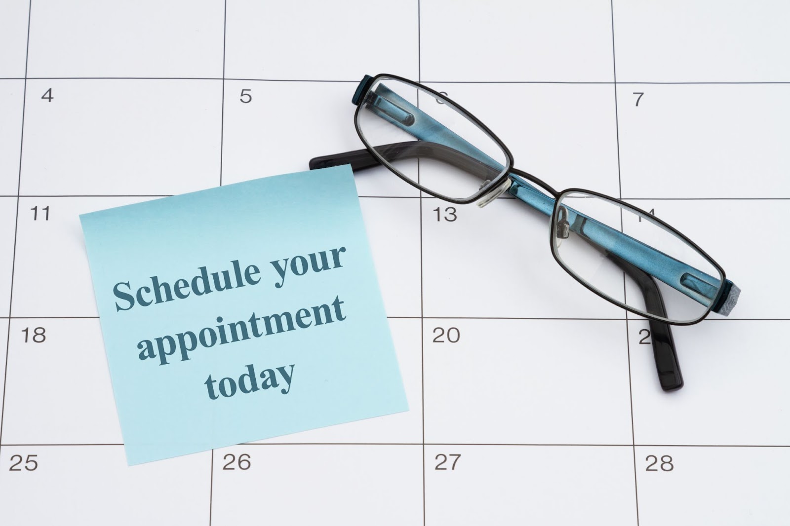 A pair of glasses and a sticky note saying “Schedule your appointment today” rest on a calendar.