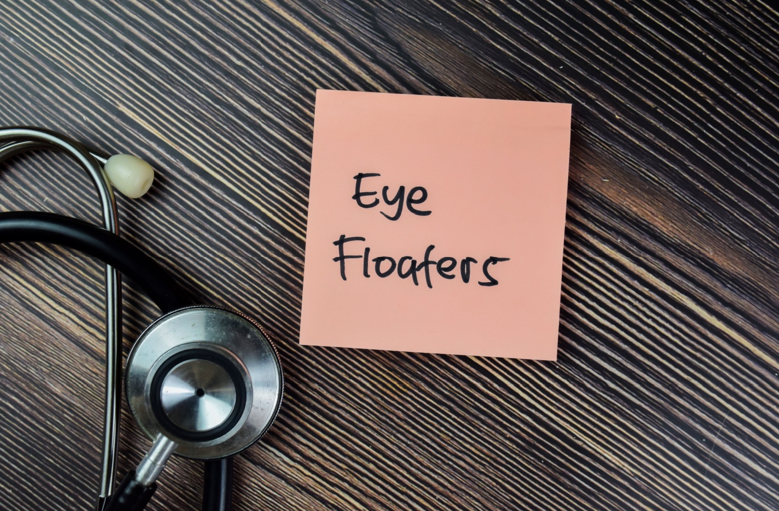 there is a sticky note on a desk that read 'eye floaters' with a stethoscope beside it.