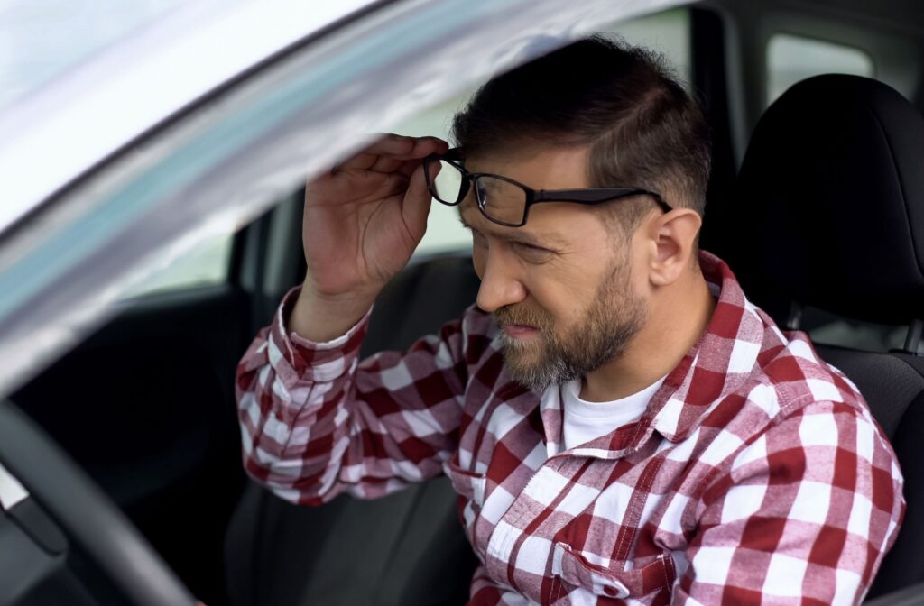 A man holding glasses and squinting while driving.