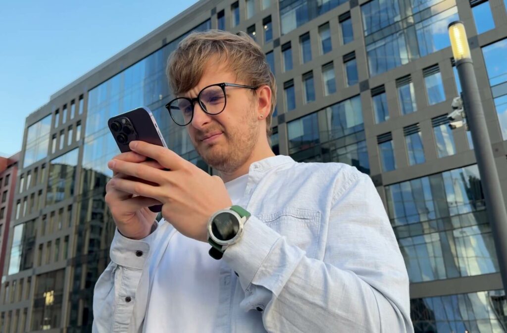 A young adult holds a smartphone close to their bespectacled face, squinting to see clearly.