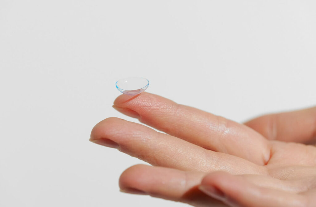 Close-up of a hand holding up a singular contact lens against a white backdrop.