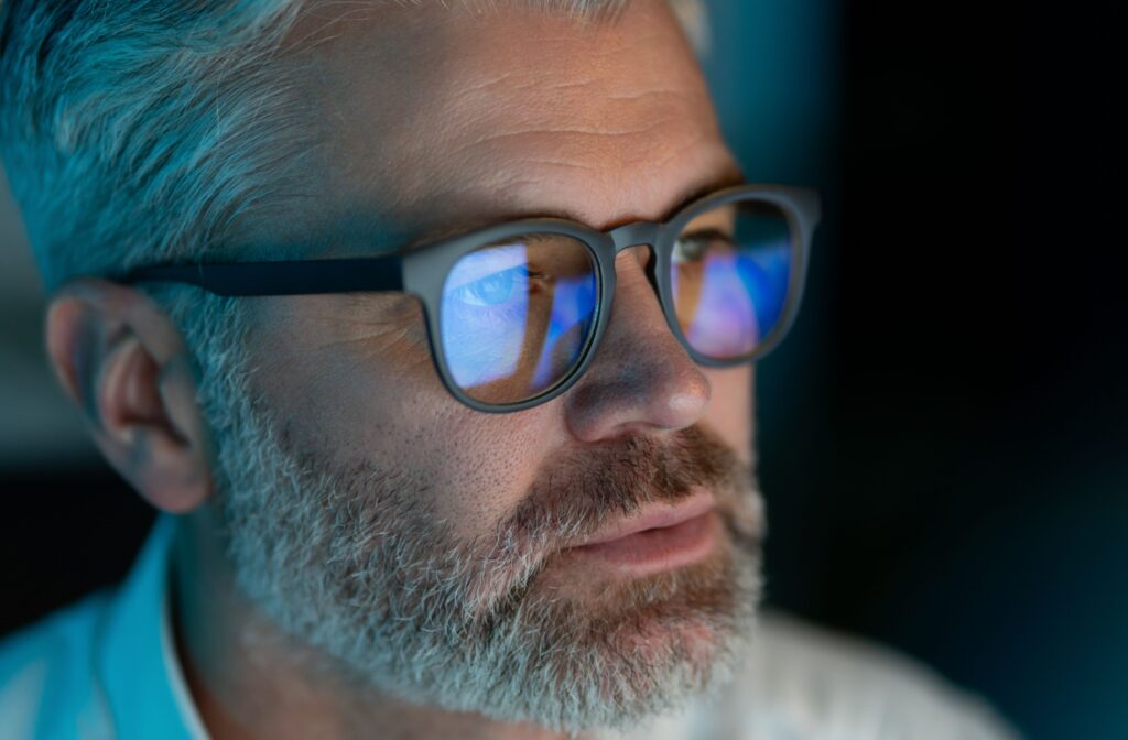 Close-up of an individual wearing black-rimmed eyeglasses with blue-light lenses. A blue sheen can be seen on the lenses