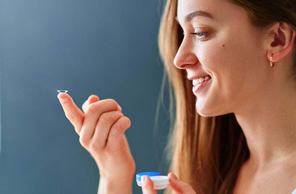 A young adult smiling with a specialty contact lens for astigmatism resting on the tip of their outstretched pointer finger.