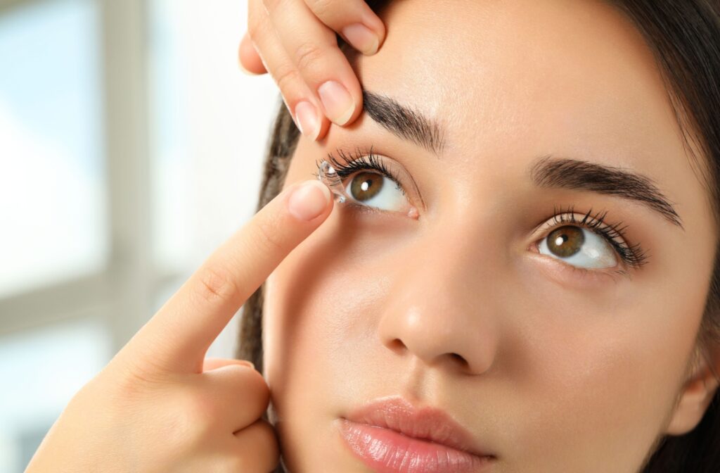 Close-up photo of a woman with brown eyes and hair putting contact lens in right eye with her finger.