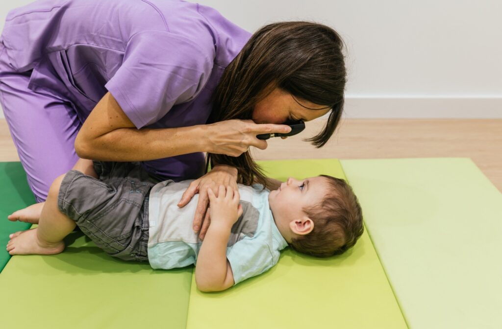 An eye doctor performs a modified eye exam on a toddler that's laying on the ground.