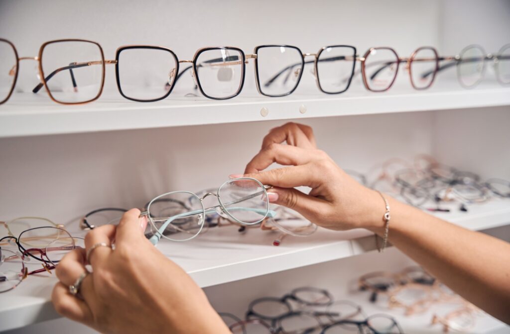 A pair of hands selecting a pair of glasses from a shelf full of eyeglasses.